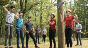 Group of corporate team members engaged in outdoor leadership challenges, wearing harnesses and helmets, participating in a team-building activity in a forest setting.