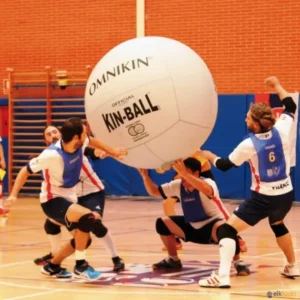 Four players engaging in a Kin-Ball game indoors, lifting a large ball.
