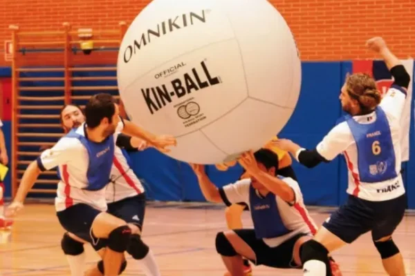 Four players engaging in a Kin-Ball game indoors, lifting a large ball.